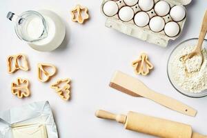 Objects and ingredients for baking, plastic molds for cookies on a white background. Flour, eggs, rolling pin, milk, butter, cream. Top view, space for text photo