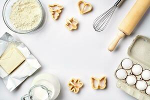 Objects and ingredients for baking, plastic molds for cookies on a white background. Flour, eggs, rolling pin, whisk, milk, butter, cream. Top view, space for text photo