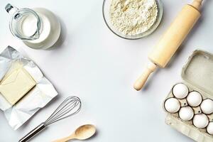 Objects and ingredients for baking, plastic molds for cookies on a white background. Flour, eggs, rolling pin, whisk, milk, butter, cream. Top view, space for text photo