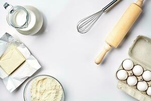 Objects and ingredients for baking, plastic molds for cookies on a white background. Flour, eggs, rolling pin, whisk, milk, butter, cream. Top view, space for text photo