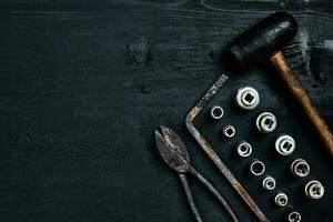 Copy space of working tools on a black wooden surface. Nippers, wrench keys, pliers, screwdriver, hammer. Top view. photo
