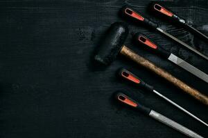 Series of many sharp steel blades and hammer on black wooden background photo
