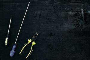 Screwdrivers, pliers and tools on a black wooden table. Top view photo