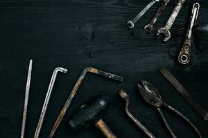 Old, rusty tools lying on a black wooden table. Hammer, chisel, metal scissors, wrench. photo