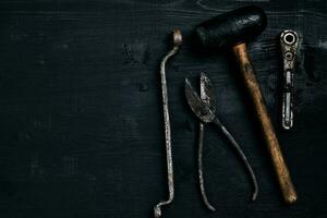 Old, rusty tools lying on a black wooden table. Hammer, chisel, metal scissors, wrench. photo