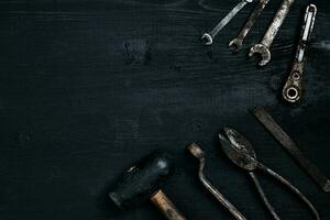 Old, rusty tools lying on a black wooden table. Hammer, chisel, metal scissors, wrench. photo