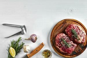 Raw beef steak with spices and ingredients for cooking on wooden cutting board and white background. photo