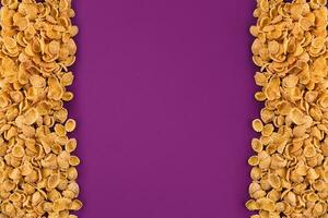 A frame lined with corn flakes. Cornflakes scattered on a purple background. Copy space photo