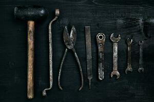 Old, rusty tools lying on a black wooden table. Hammer, chisel, metal scissors, wrench. photo