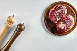 Raw beef steak with spices and ingredients for cooking on wooden cutting board and white background. photo