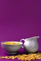Bowl with corn flakes, jug of milk on purple background. oncept of a healthy breakfast photo