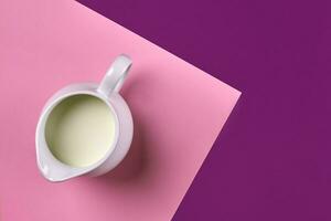 White ceramic jug of fresh milk on purple and pink background. Top view photo