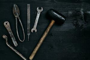 Old, rusty tools lying on a black wooden table. Hammer, chisel, metal scissors, wrench. photo