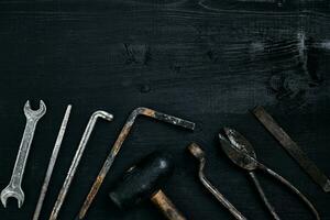 Old, rusty tools lying on a black wooden table. Hammer, chisel, metal scissors, wrench. photo