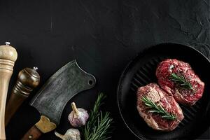 Fresh raw meat. A piece of beef tenderloin on grill pan, with a cutting ax, with spices for cooking on black stone table. Copy space photo