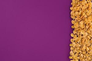 A frame lined with corn flakes. Cornflakes scattered on a purple background. Copy space photo