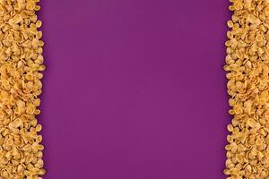 A frame lined with corn flakes. Cornflakes scattered on a purple background. Copy space photo