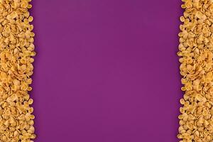 A frame lined with corn flakes. Cornflakes scattered on a purple background. Copy space photo