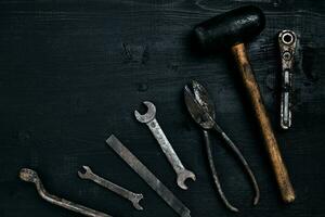 Old, rusty tools lying on a black wooden table. Hammer, chisel, metal scissors, wrench. photo