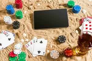Gambling on vacation concept - white sand with seashells , colored poker chips and cards. Top view photo