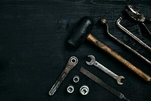 Old, rusty tools lying on a black wooden table. Hammer, chisel, metal scissors, wrench. photo