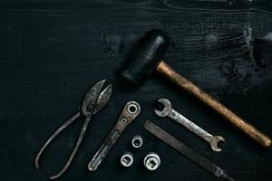 Old, rusty tools lying on a black wooden table. Hammer, chisel, metal scissors, wrench. photo