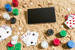 Gambling on vacation concept - white sand with seashells , colored poker chips and cards. Top view photo