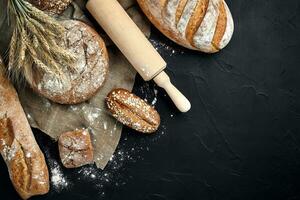 Top view of baguette, baked bread, flour and wheat spikes composition with wheat flour sprinkled around on a dark background photo