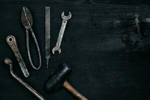 Old, rusty tools lying on a black wooden table. Hammer, chisel, metal scissors, wrench. photo