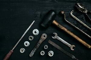 Old, rusty tools lying on a black wooden table. Hammer, chisel, metal scissors, wrench. photo