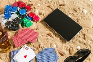 Gambling on vacation concept - white sand with seashells , colored poker chips and cards. Top view photo