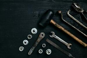 Old, rusty tools lying on a black wooden table. Hammer, chisel, metal scissors, wrench. photo