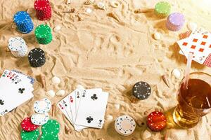 Gambling on vacation concept - white sand with seashells , colored poker chips and cards. Top view photo