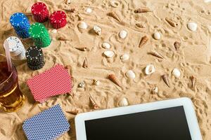 Gambling on vacation concept - white sand with seashells , colored poker chips and cards. Top view photo