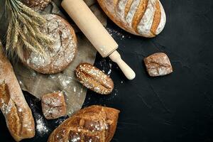 parte superior ver de junquillo, horneado pan, harina y trigo Picos composición con trigo harina rociado alrededor en un oscuro antecedentes foto