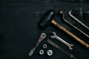 Old, rusty tools lying on a black wooden table. Hammer, chisel, metal scissors, wrench. photo