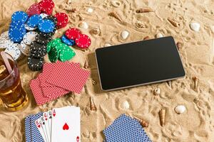 Online poker game on the beach with digital tablet and stacks of chips. Top view photo