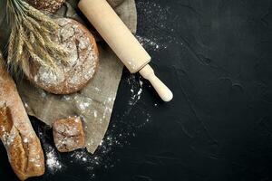 Top view of baguette, baked bread, flour and wheat spikes composition with wheat flour sprinkled around on a dark background photo