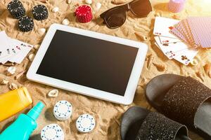 Online poker game on the beach with digital tablet and stacks of chips. Top view photo