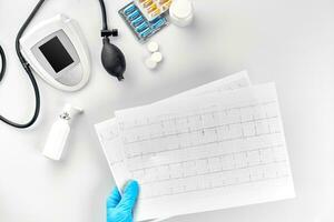 parte superior ver de del doctor mano con resultado de el encuesta, digital sangre presión monitor en blanco mesa foto