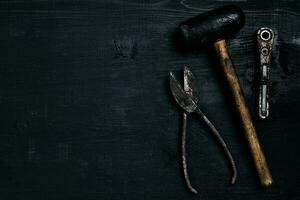 Old, rusty tools lying on a black wooden table. Hammer, chisel, metal scissors, wrench. photo