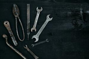 viejo, oxidado herramientas acostado en un negro de madera mesa. martillo, cincel, metal tijeras, llave inglesa. foto