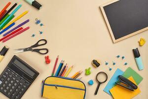 Flat lay photo of workspace desk with school accessories or office supplies on pink background.