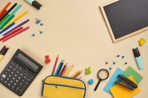 Flat lay photo of workspace desk with school accessories or office supplies on pink background.