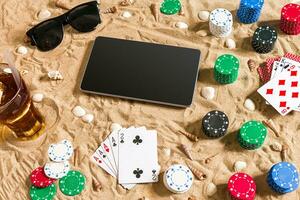 Gambling on vacation concept - white sand with seashells , colored poker chips and cards. Top view photo