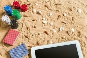 Gambling on vacation concept - white sand with seashells , colored poker chips and cards. Top view photo