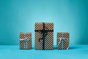 Different sizes, colorful, striped, brown paper gift boxes tied with ribbons and bows on a blue surface and background. Close-up, copy space. photo