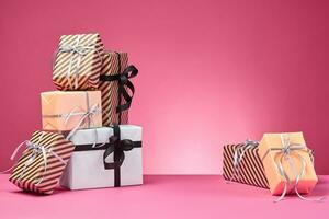 Different sizes, colorful, striped and plain paper gift boxes tied with ribbons and bows on a pink surface and background. Close-up, copy space. photo