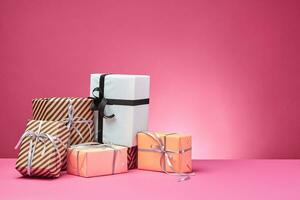 Different sizes, colorful, striped and plain paper gift boxes tied with ribbons and bows on a pink surface and background. Close-up, copy space. photo