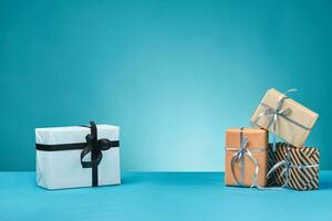 Different sizes, colorful, striped and plain paper gift boxes tied with ribbons and bows on a blue surface and background. Close-up, copy space. photo